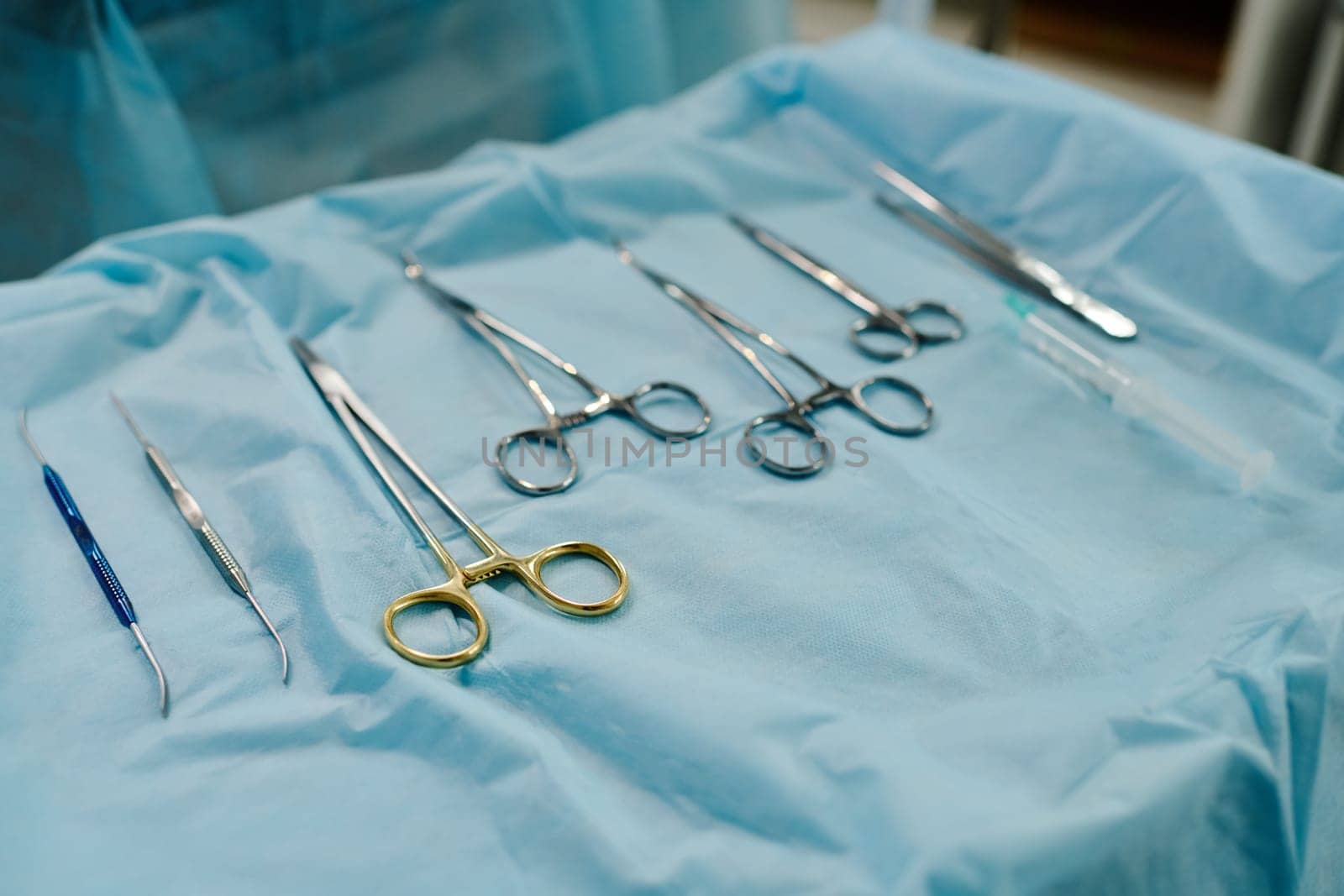 Set of sterile steel medical tools for carrying out surgical operation lying on blue napkin on push cart or table prepared for procedure