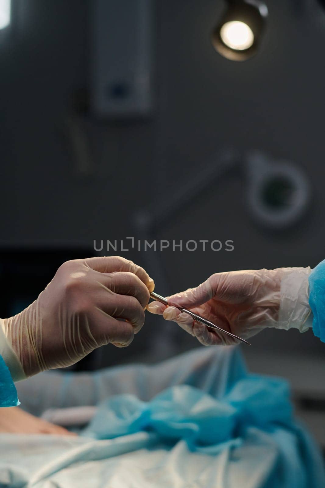 Gloved hand of assistant passing sterile scalpel or some other surgical tool against patient covered with napkin during operation