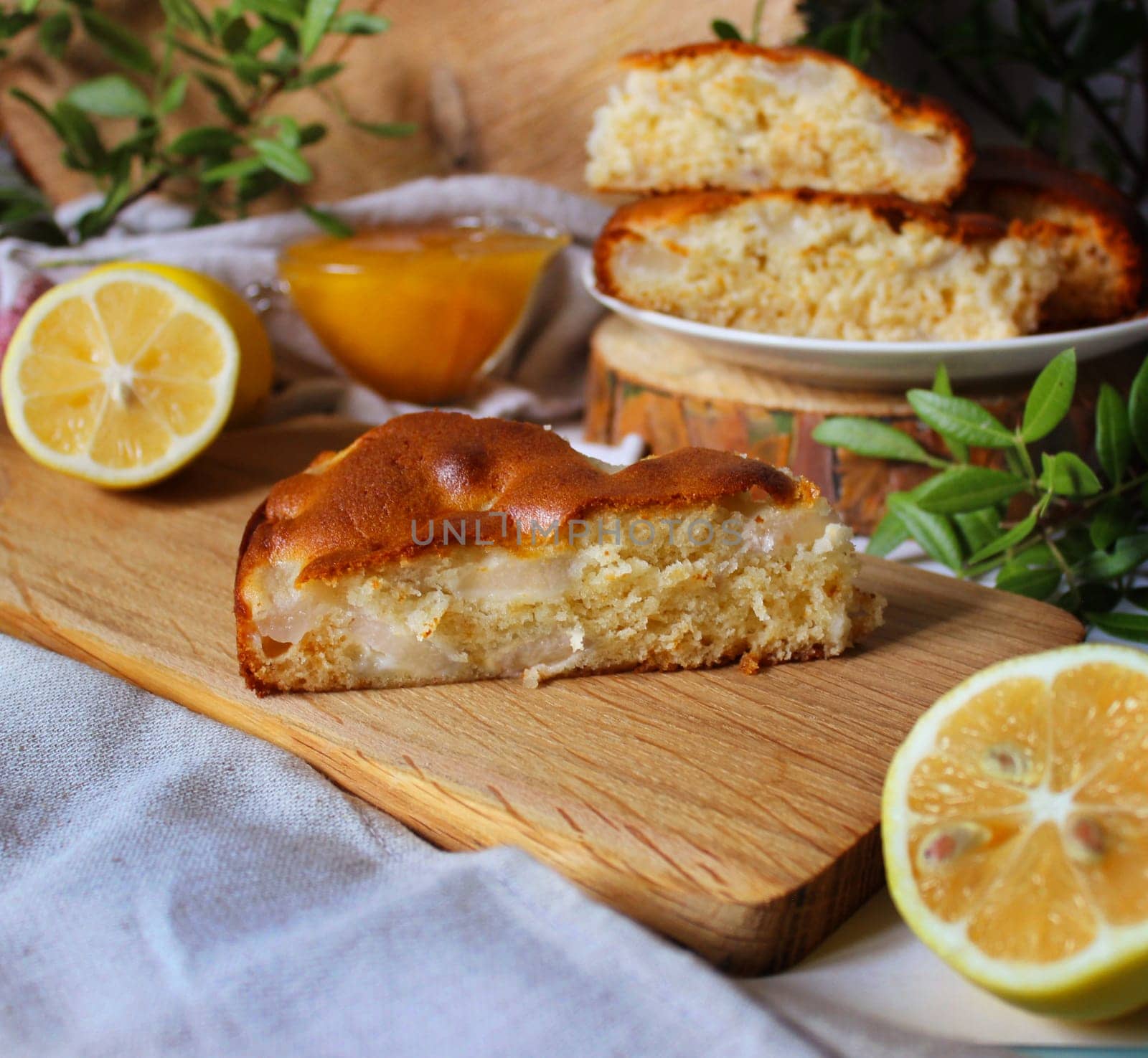 A piece of apple pie on a wooden board with lemon slices and honey on a background of green twigs and wooden blocks