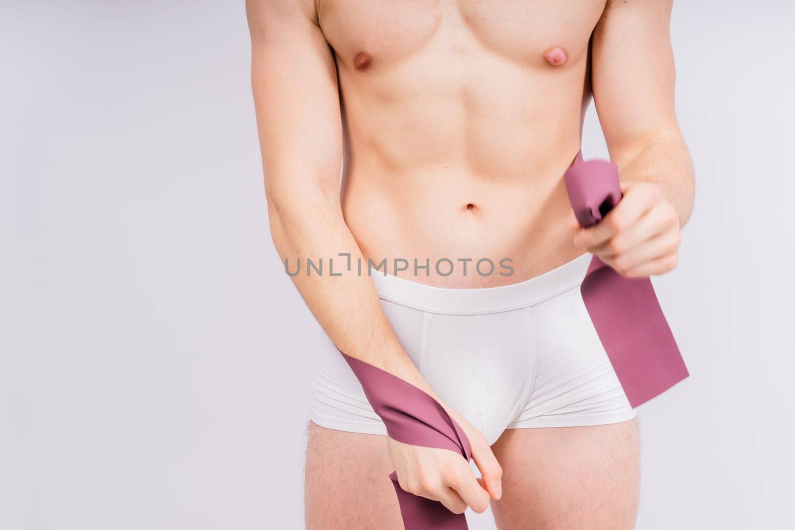 Athlete with muscular body in white panties is doing physical exercises with rubber