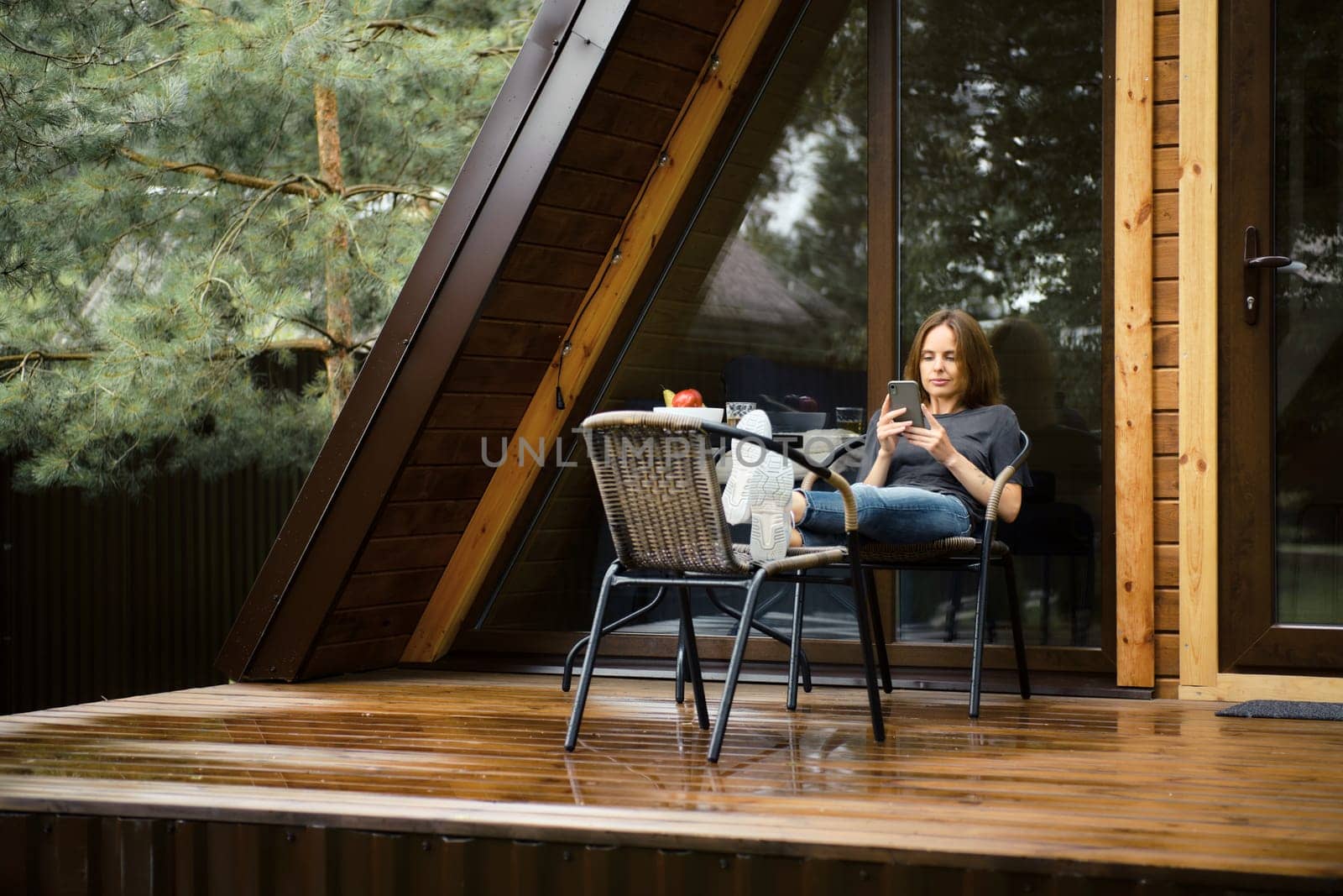 Cute woman with smartphone on terrace of her a-frame cabin