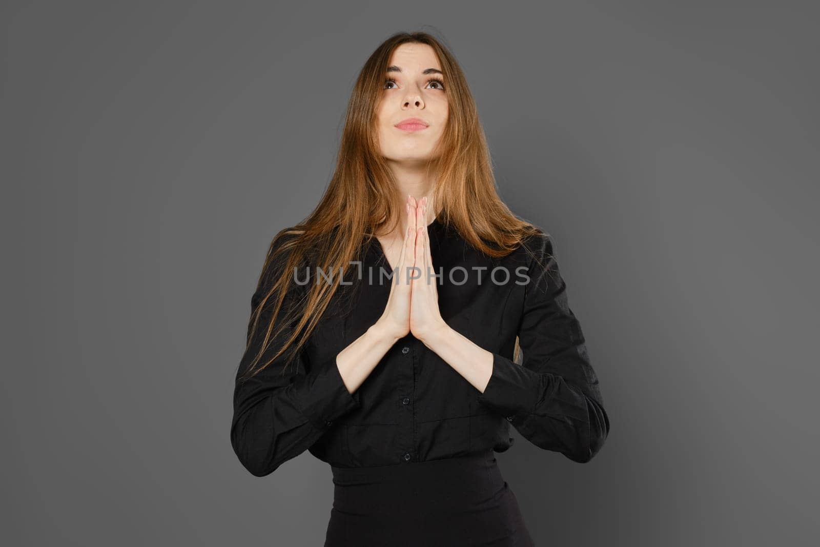 Woman holds hands in praying gesture, looking up