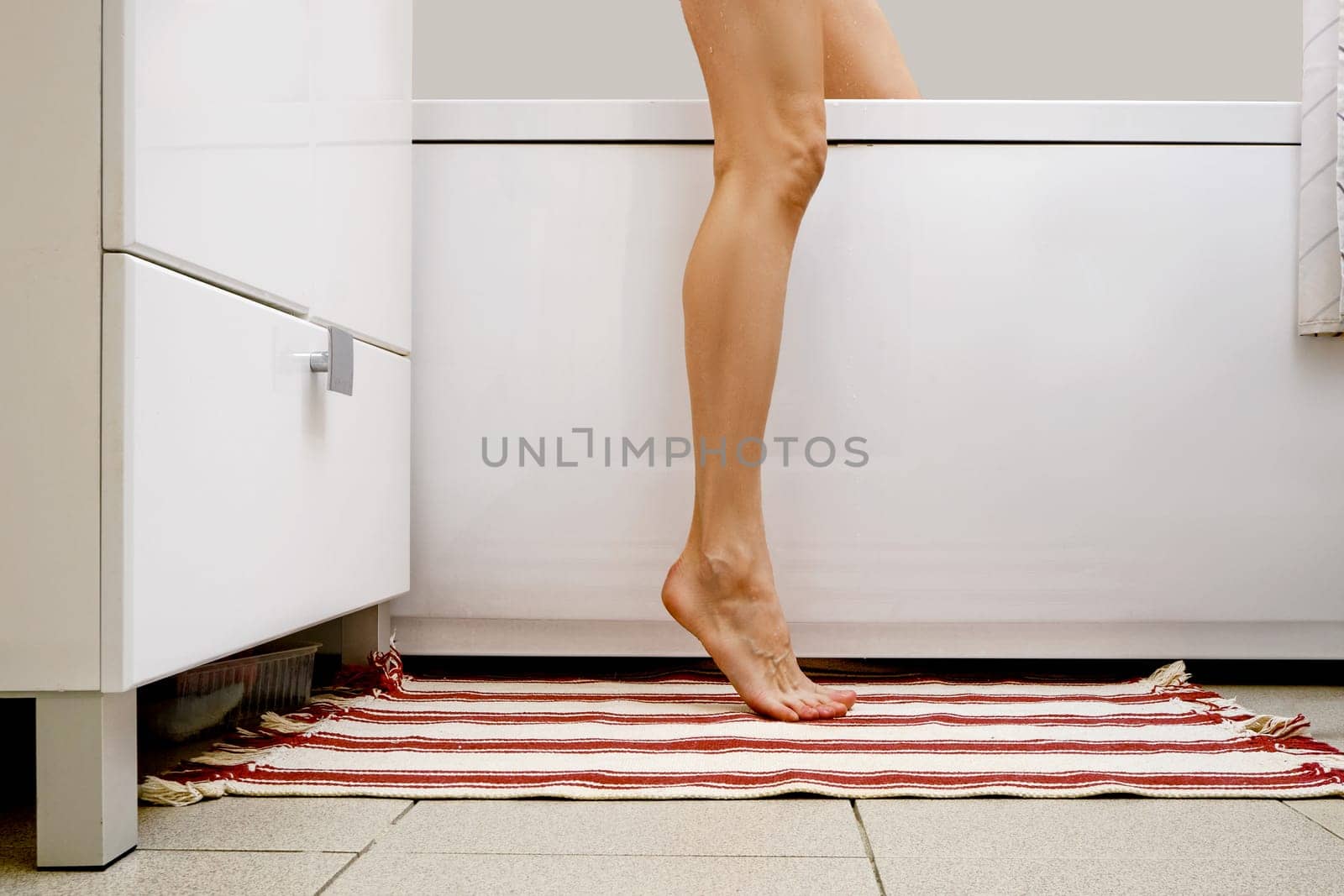 Slim leg of unrecognizable woman on a carpet near bathtub