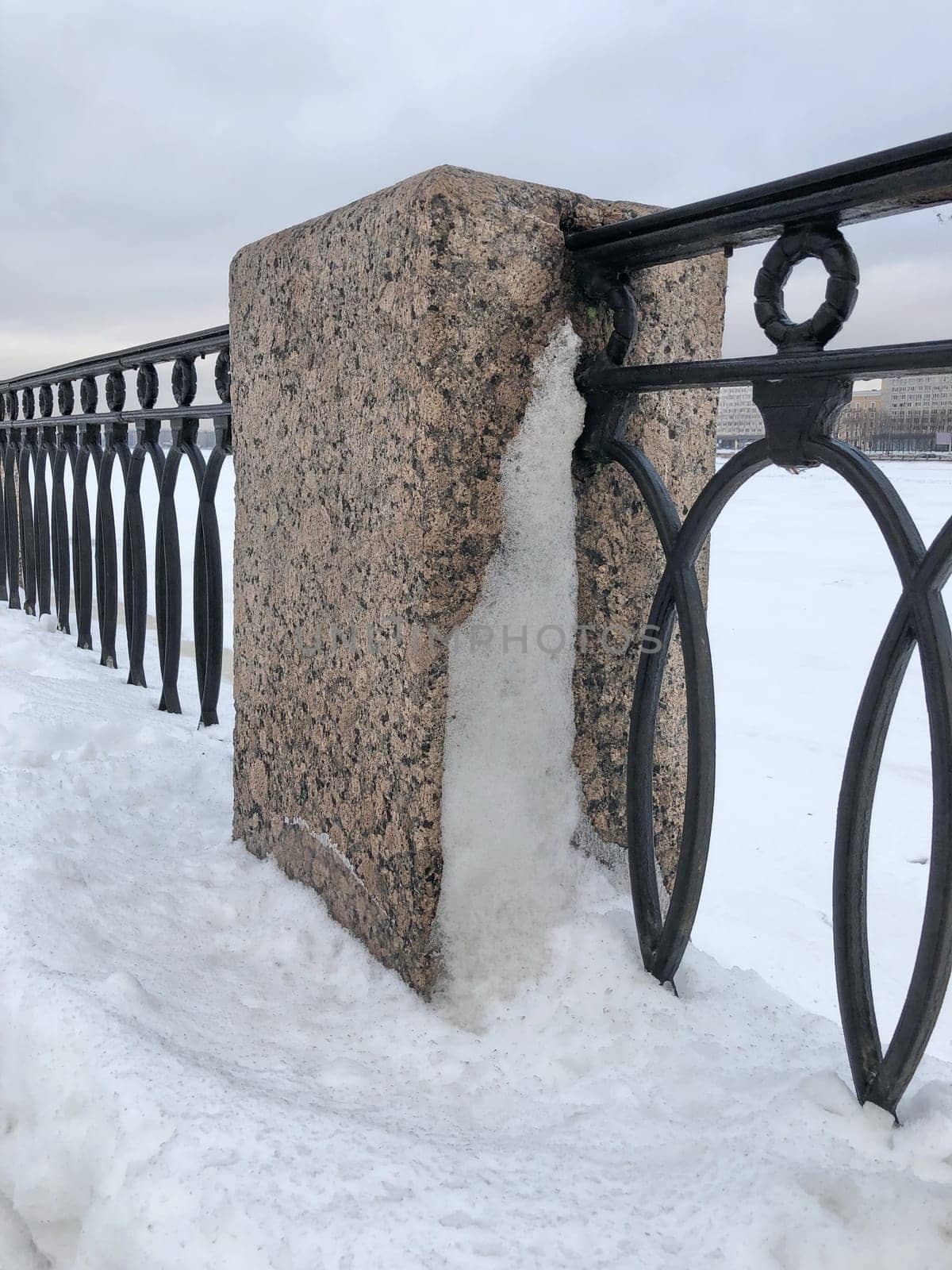 granite pillar and cast iron embankment fence in the snow, winter landscape St. Petersburg