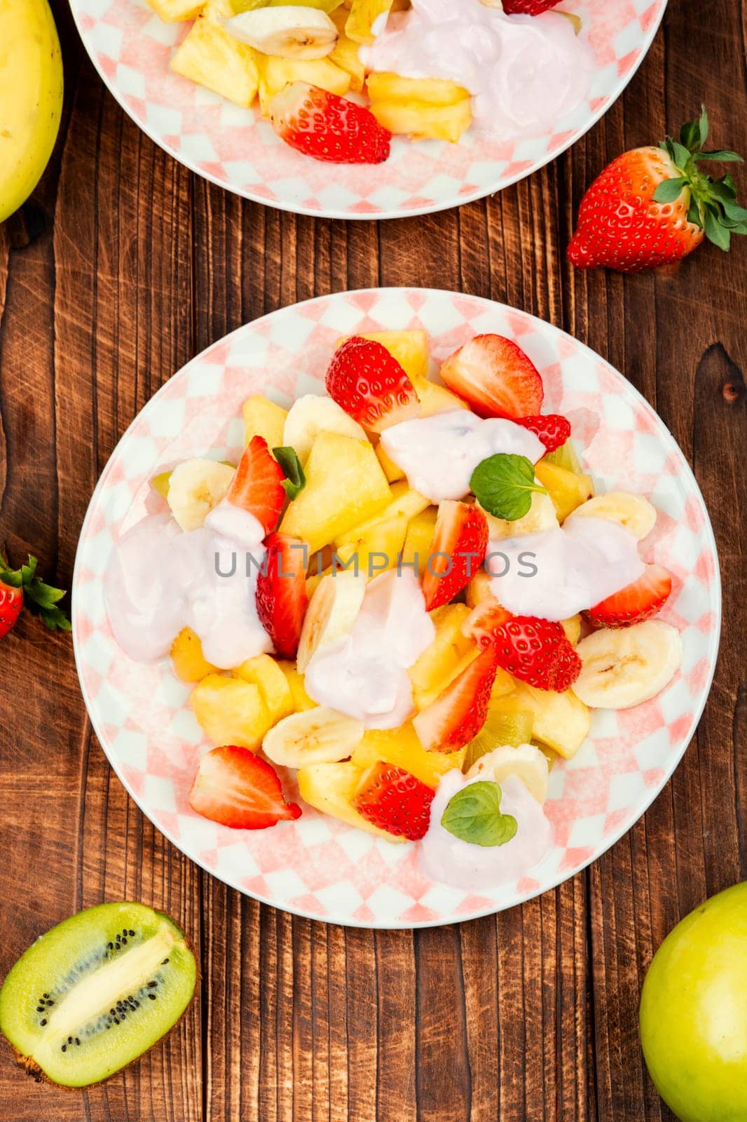 Delicious fruit salad of strawberries, pineapple, kiwi and yogurt on old rustic wooden table.