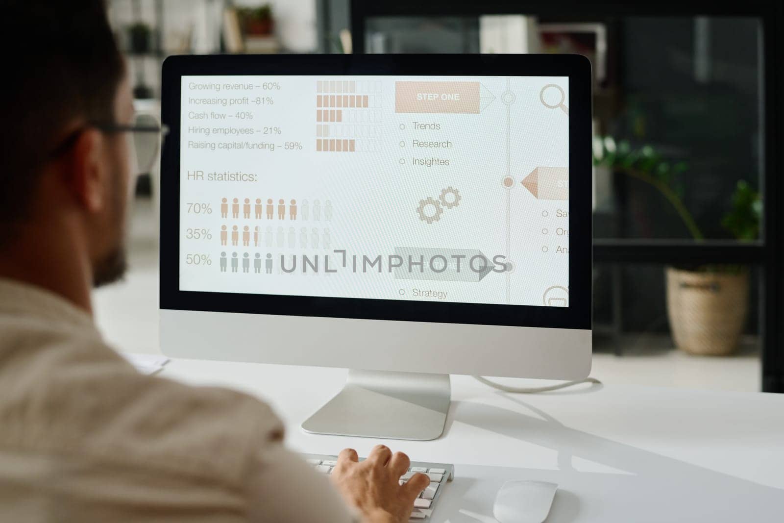 Screen of desktop computer with statistic data standing on workplace of young analyst or manager typing on keyboard during work