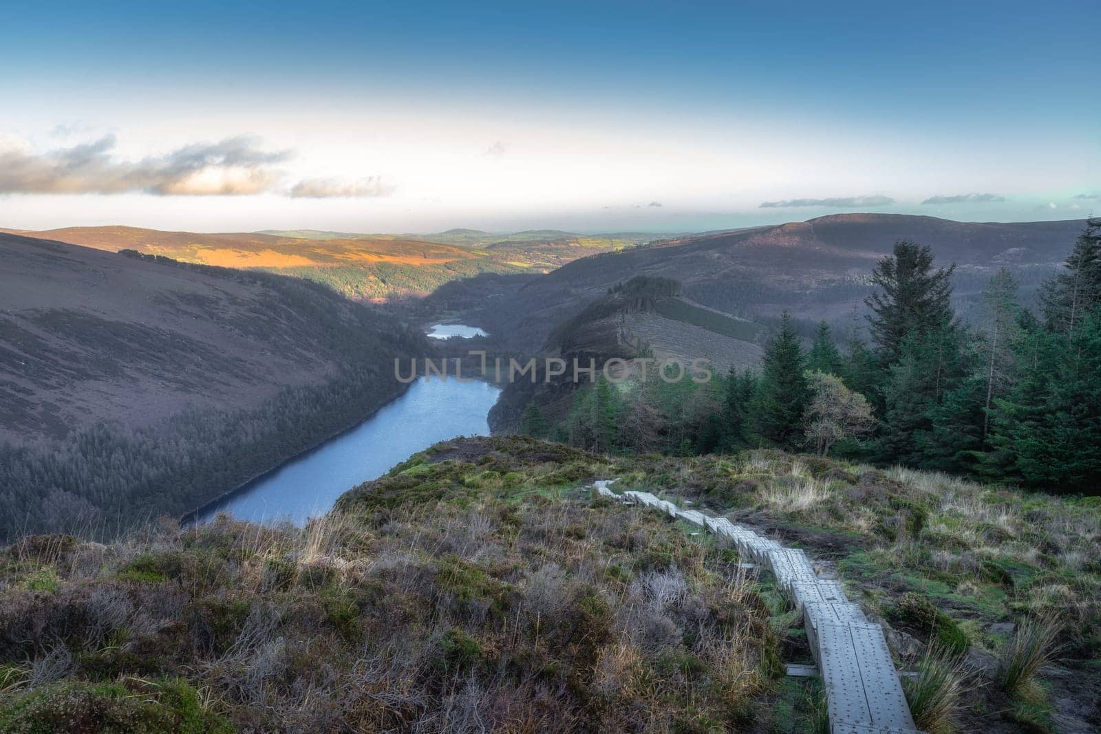 Wooden steps of a boardwalk on the top of a mountain with scenic view on Glendalough lakes and forest. Hiking in Wicklow Mountains, Ireland