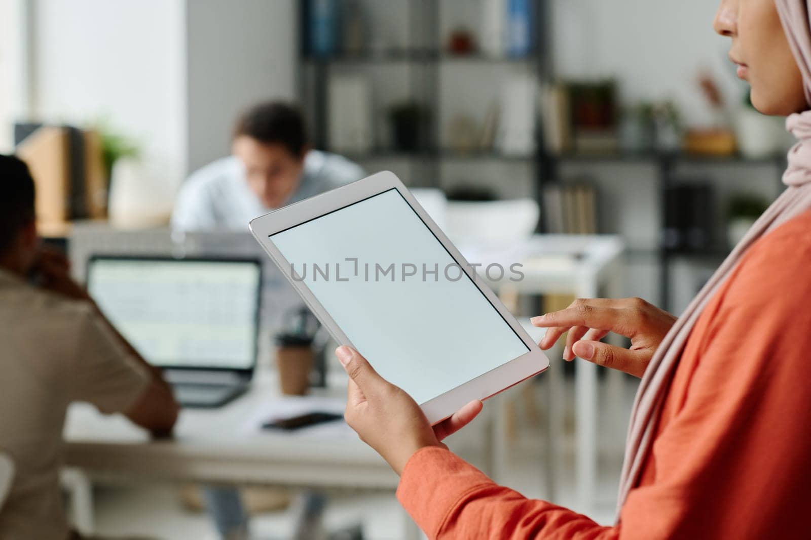 Tablet with blank screen in hands of young Muslim female manager standing in front of camera in coworking space