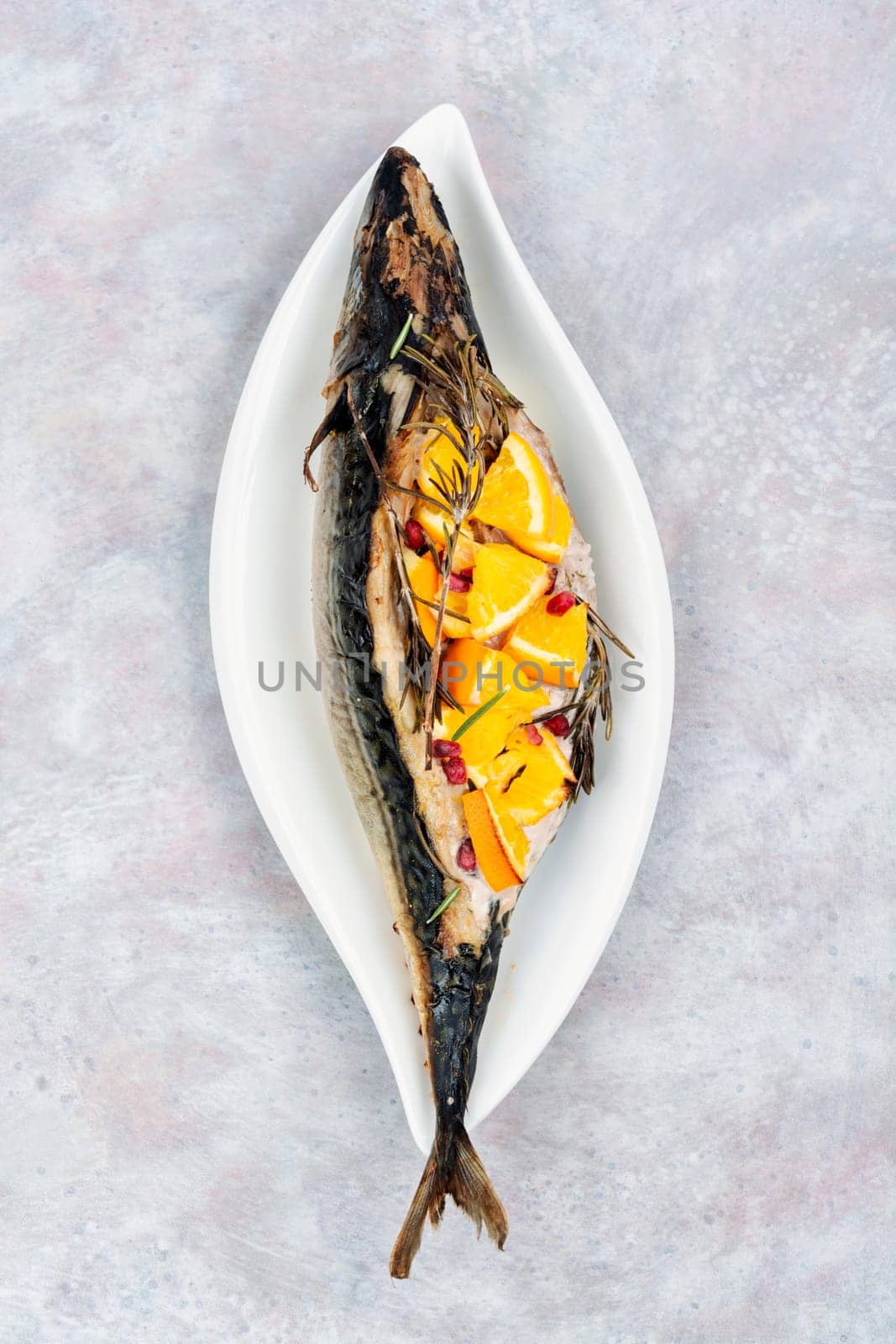 Whole mackerel fish baked with oranges and rosemary served on a stylish plate.