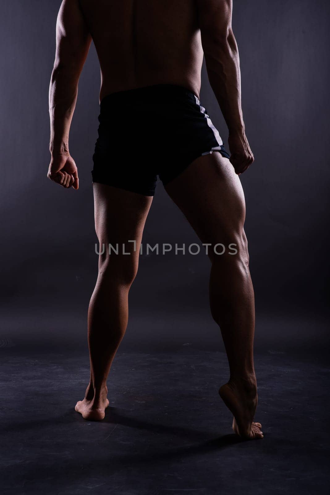 Muscular male legs, man in a studio, dark background