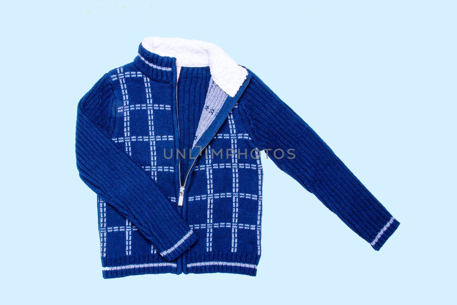 Autumn and winter jacket. A dark blue woolen knitted cardigan or pullover with a white checkered pattern on light blue background. Kids cozy warm jumper or  sweater fashion.