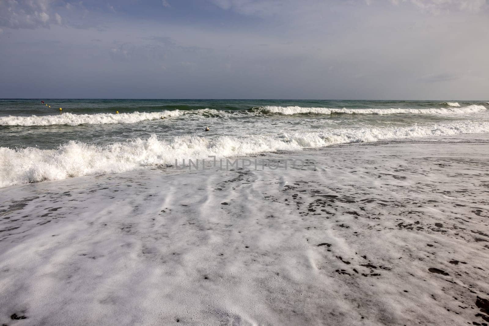 Foamy sea waves on the sandy beach of Bajondillo in Torremolinos, Malaga, Costa del Sol, Spain