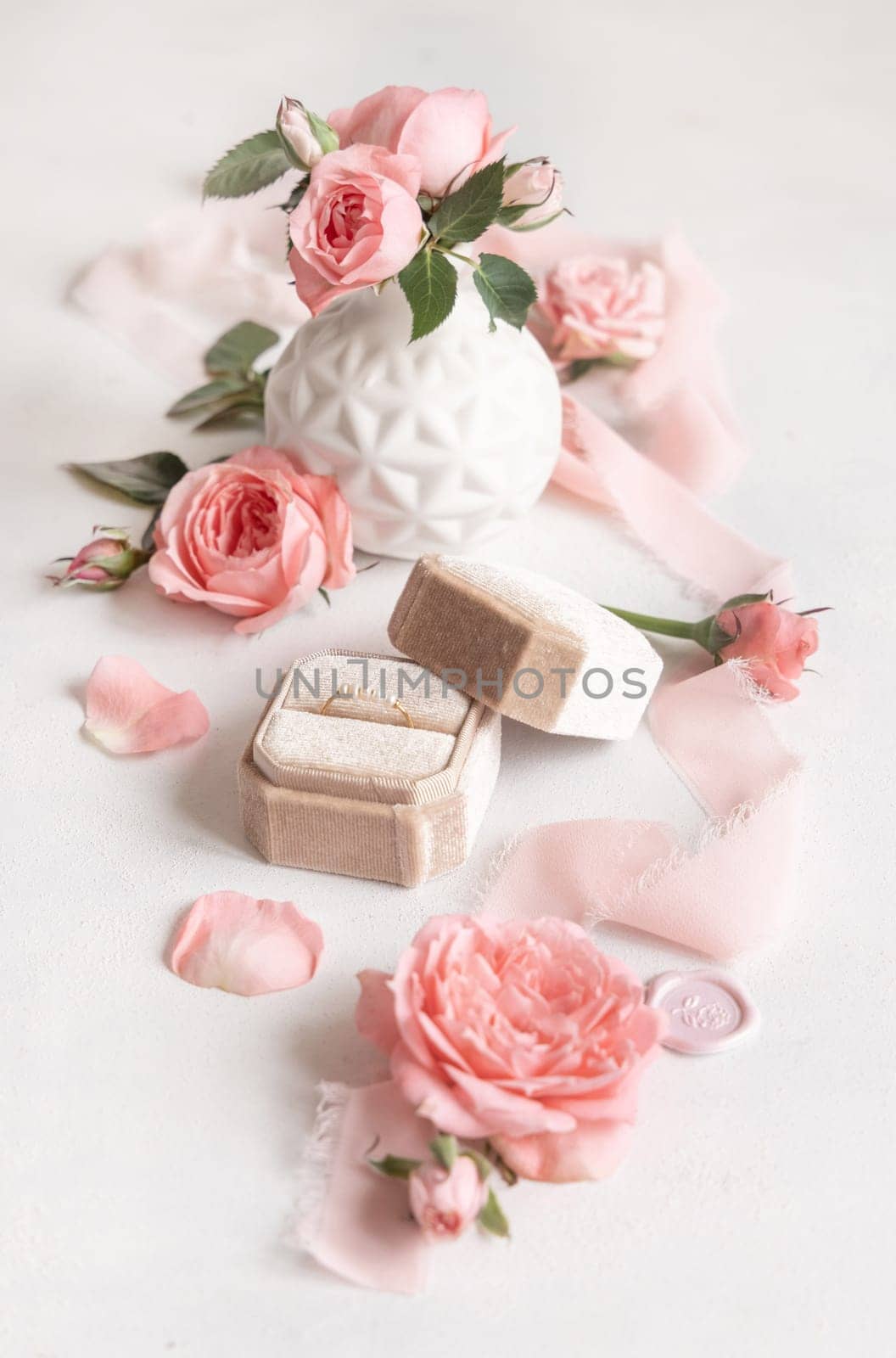 Engagement ring in a cream velvet box near light pink roses, buds and silk ribbons close up, romantic wedding preparations. Marriage proposal concept, valentines day scene