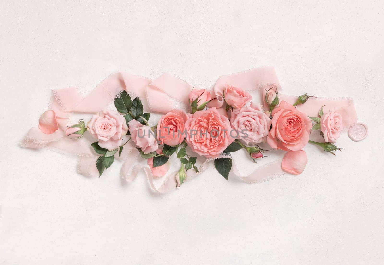 Romantic falt lay with light pink roses, petals and buds, green leaves and silk ribbons top view on white textured table . Mother's day or valentine's day concept, spring mood