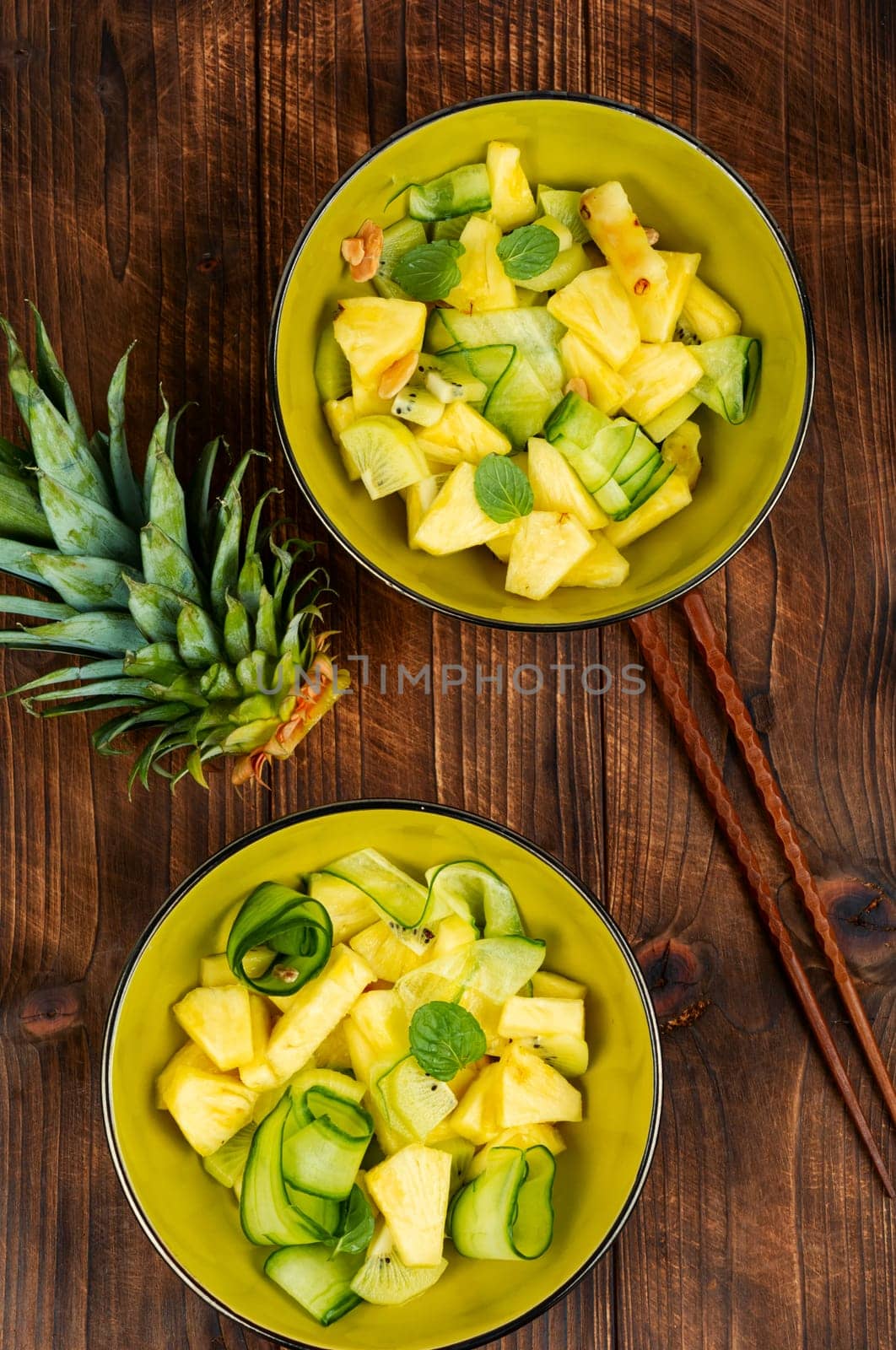 Appetizing salad with pineapple, cucumber and nuts. Healthy eating on rustic wooden table. Flat lay.