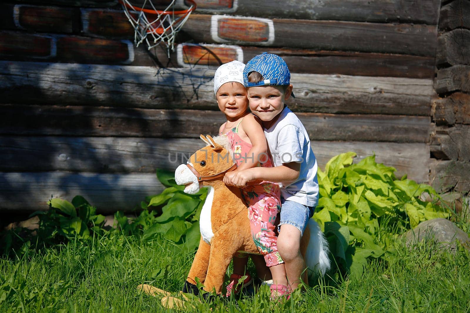 On a summer day, a girl and a boy swing on a toy horse with a white mane close-up on the street