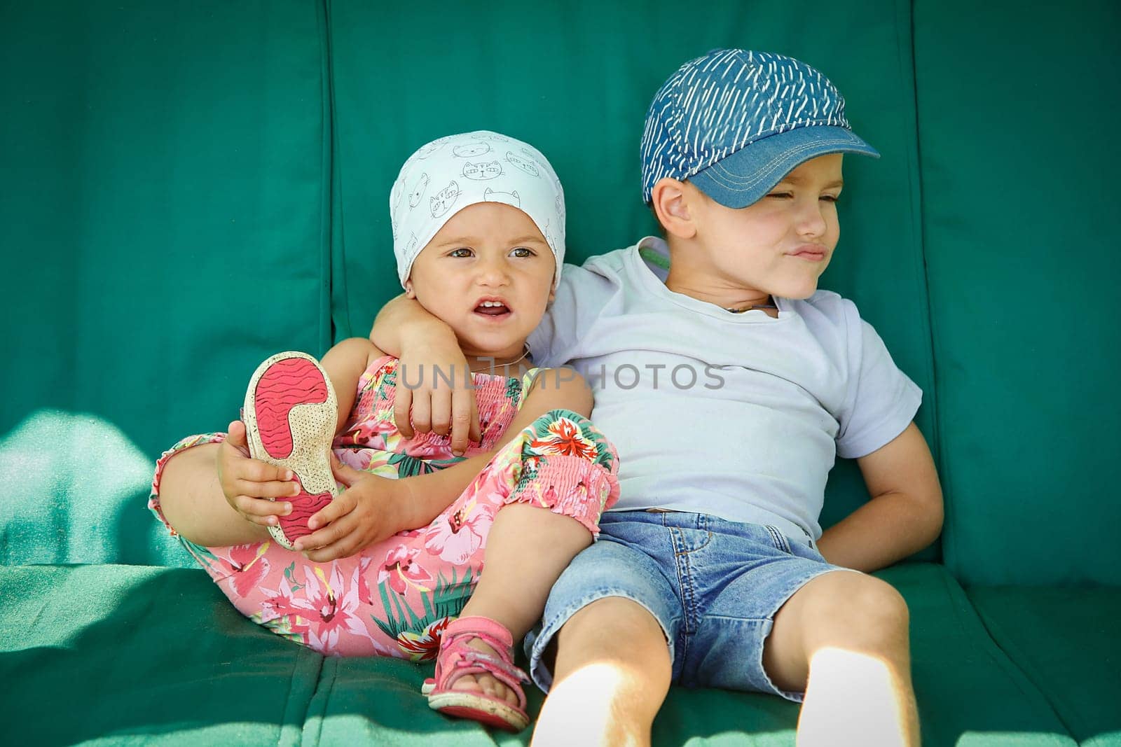 Boy and girl sitting and hugging on the green garden swing in the summer at the cottage
