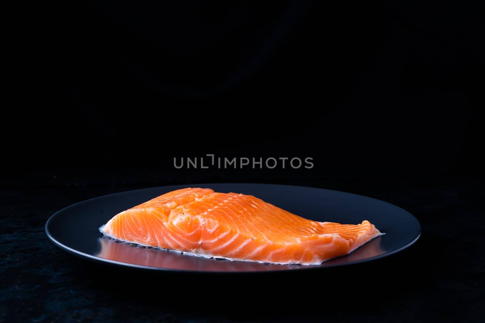 Raw salmon filet with rosemary and spices on a plate, black stone background. Top view, flat lay