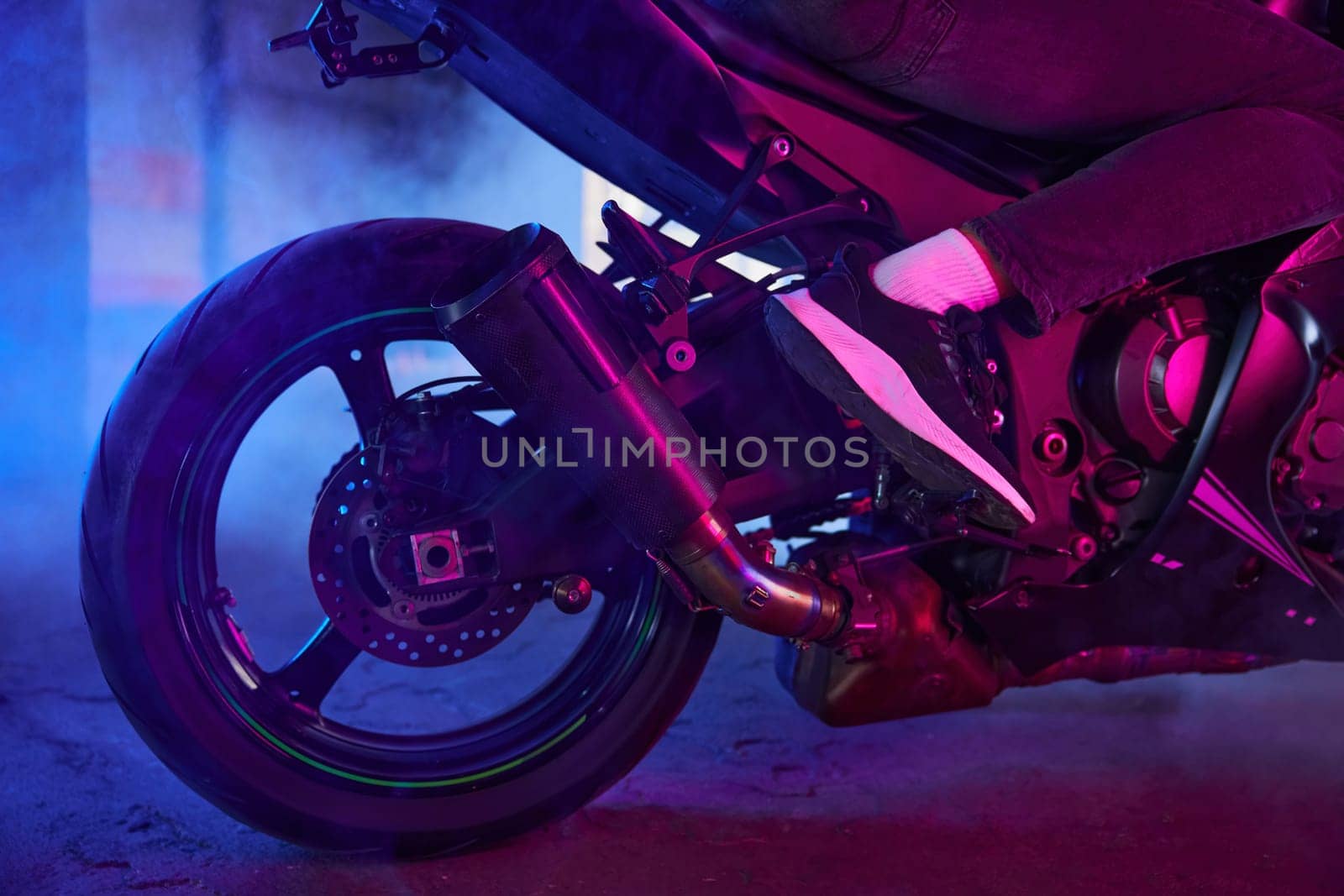 Sport motorcycle wheel view from back in neon light and smoke. Street racing training at driving school motordrome for practice