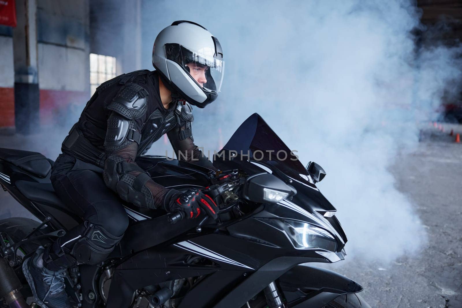 Biker wearing protective helmet and uniform for speed riding at training class of motordrome of professional driving school