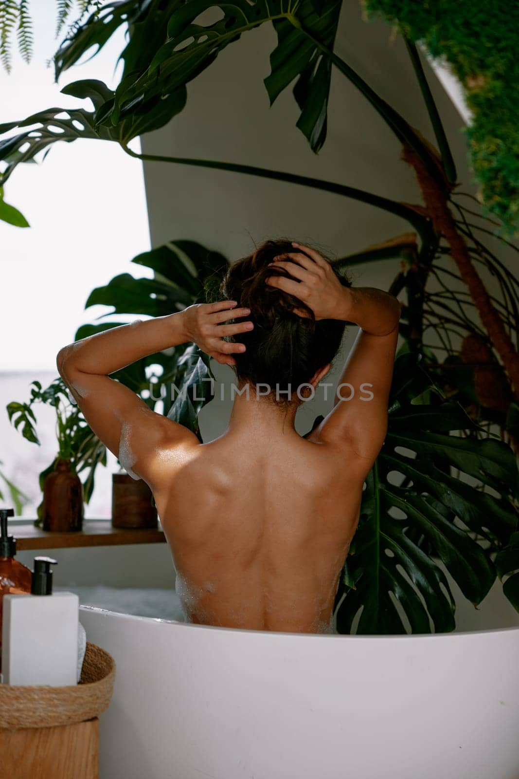 View from back on beautiful woman massaging neck applying natural organic body lotion while taking bath at home. Relax time, stress relief and spa procedure