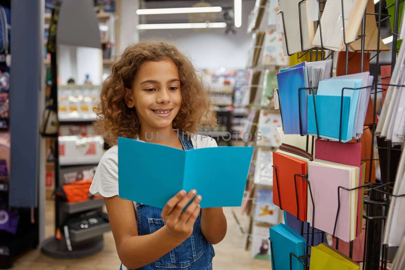 Portrait of preteen girl child at stationery shop. Cute kid reading postcard at showcase stand choosing greeting card for school friends