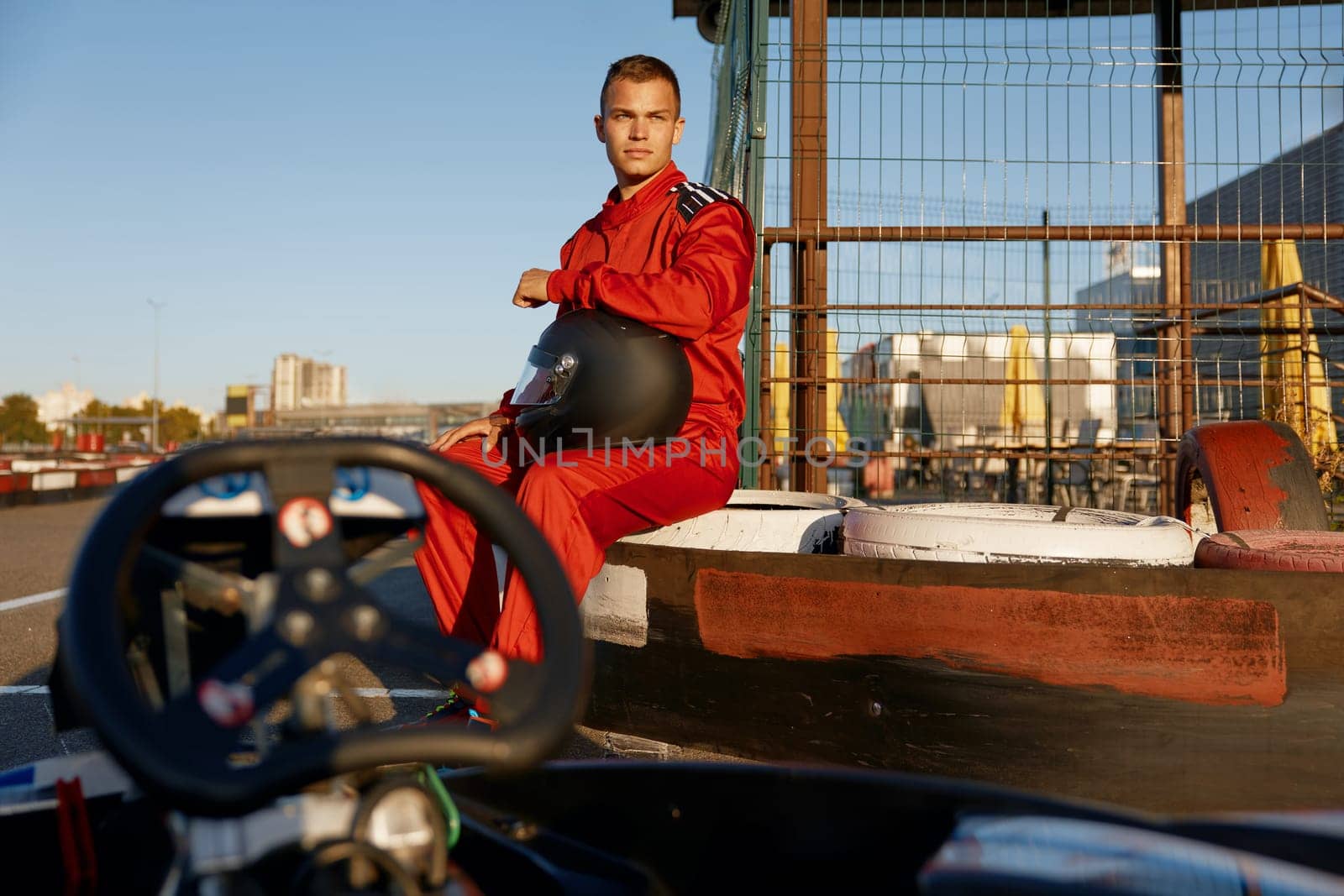 Handsome young sportsman go-cart racer in sportswear relaxing taking break before competition. Motorsport hobby