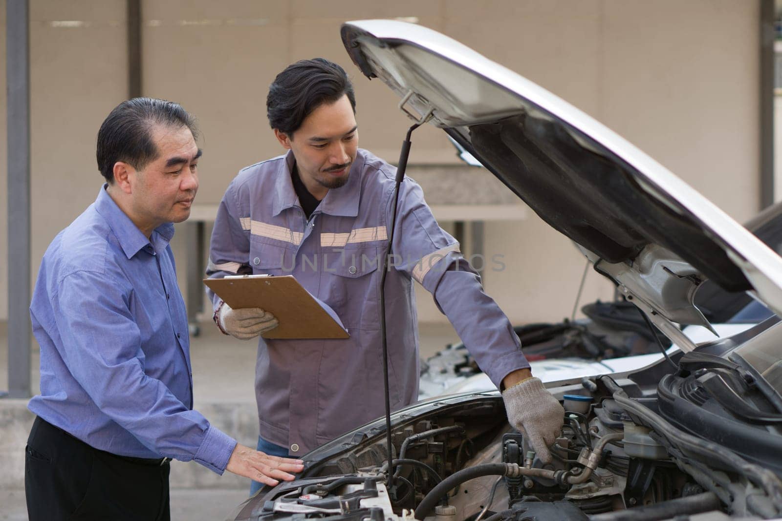 Two guys are standing by a car with the hood open, staring at the engine inside.