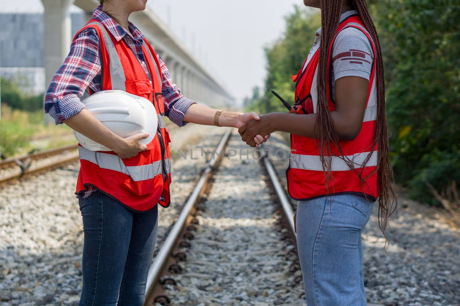 Two women wearing hard hats are shaking hands on some railroad tracks.