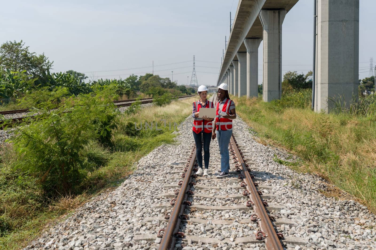 Two people are standing on railroad tracks and looking at laptop computer together.