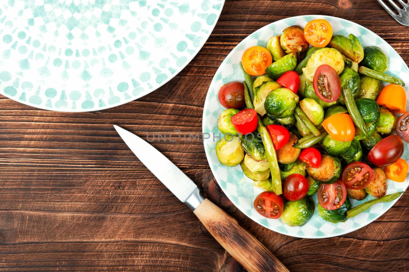 Salad of roasted brussels sprouts, tomatoes and green beans on a rustic wooden table. Flat lay with copy space.
