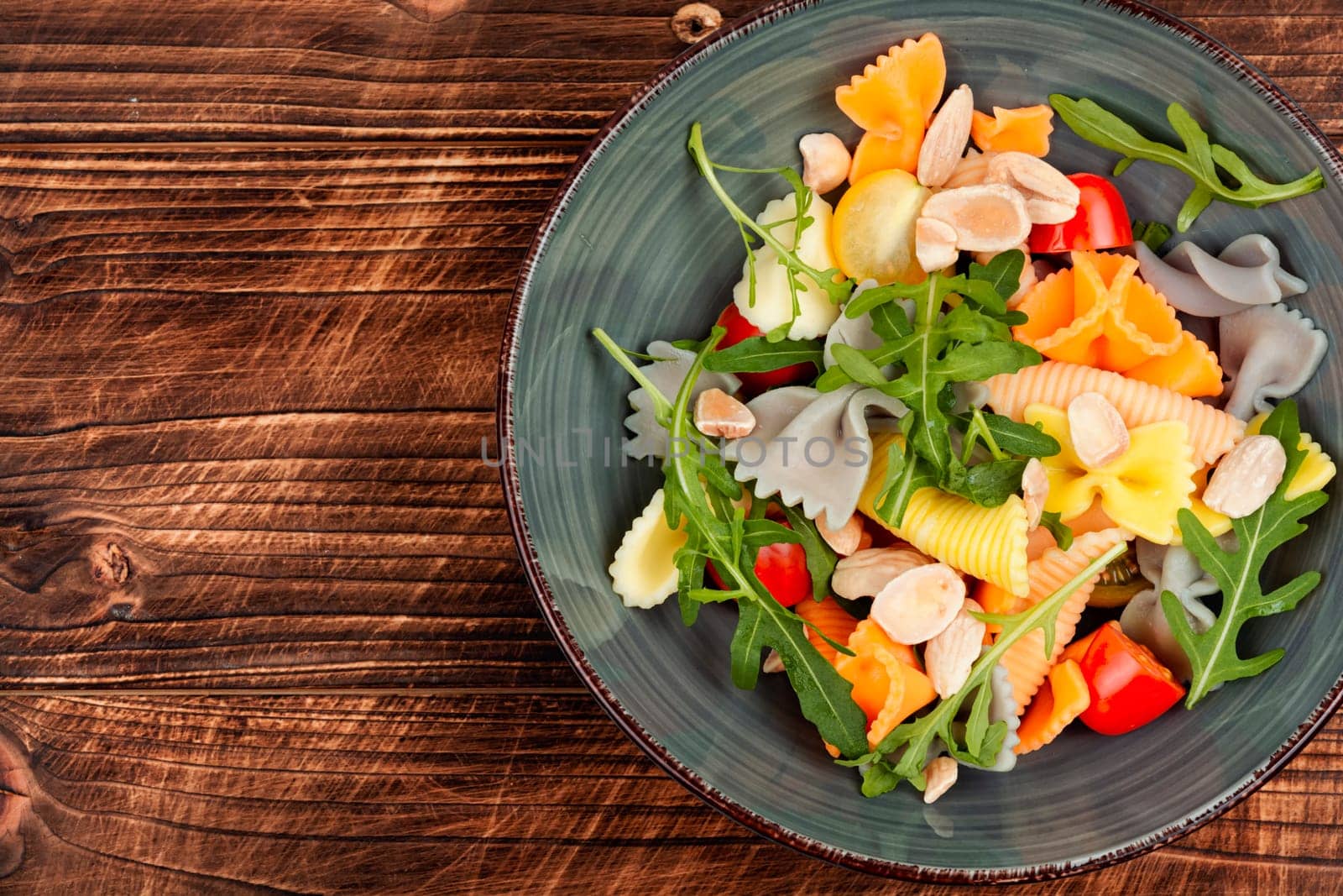 Salad with fresh tomatoes, herbs and pasta in a plate on a dark wooden table .
