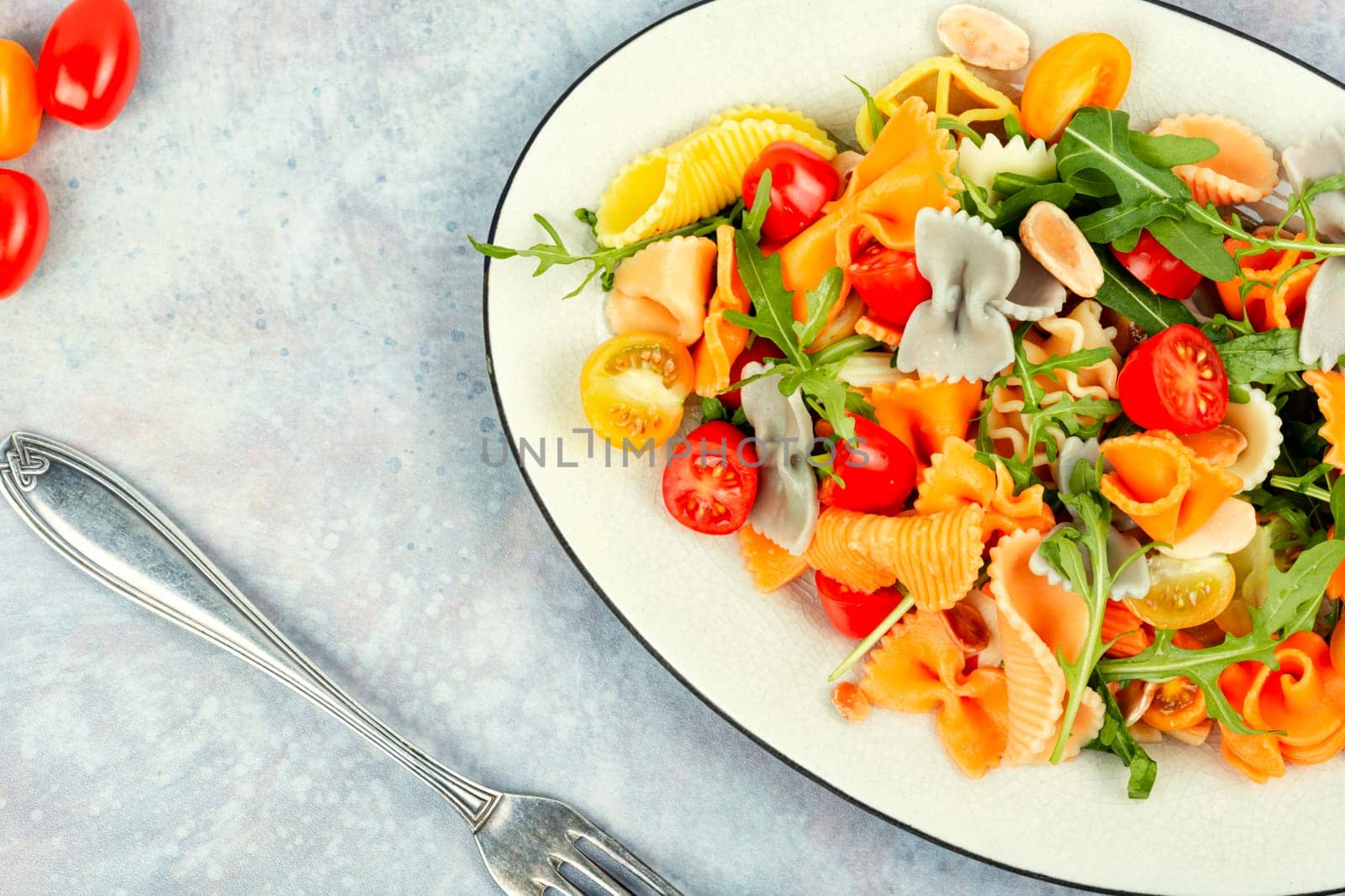 Salad with fresh tomatoes, greens and pasta on a plate.