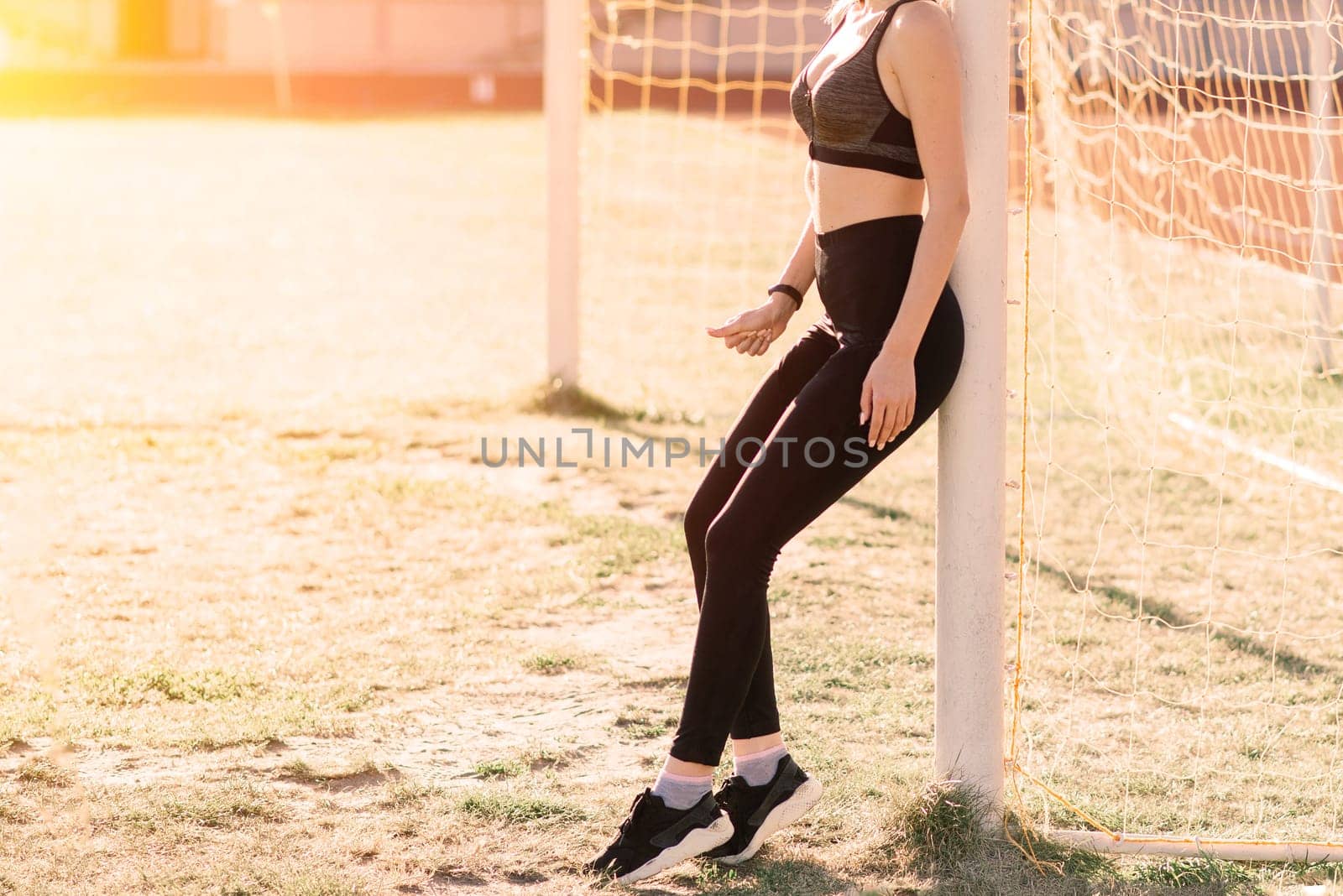 A female coach with dark hair stands on red running track of stadium, dressed in sports uniform.