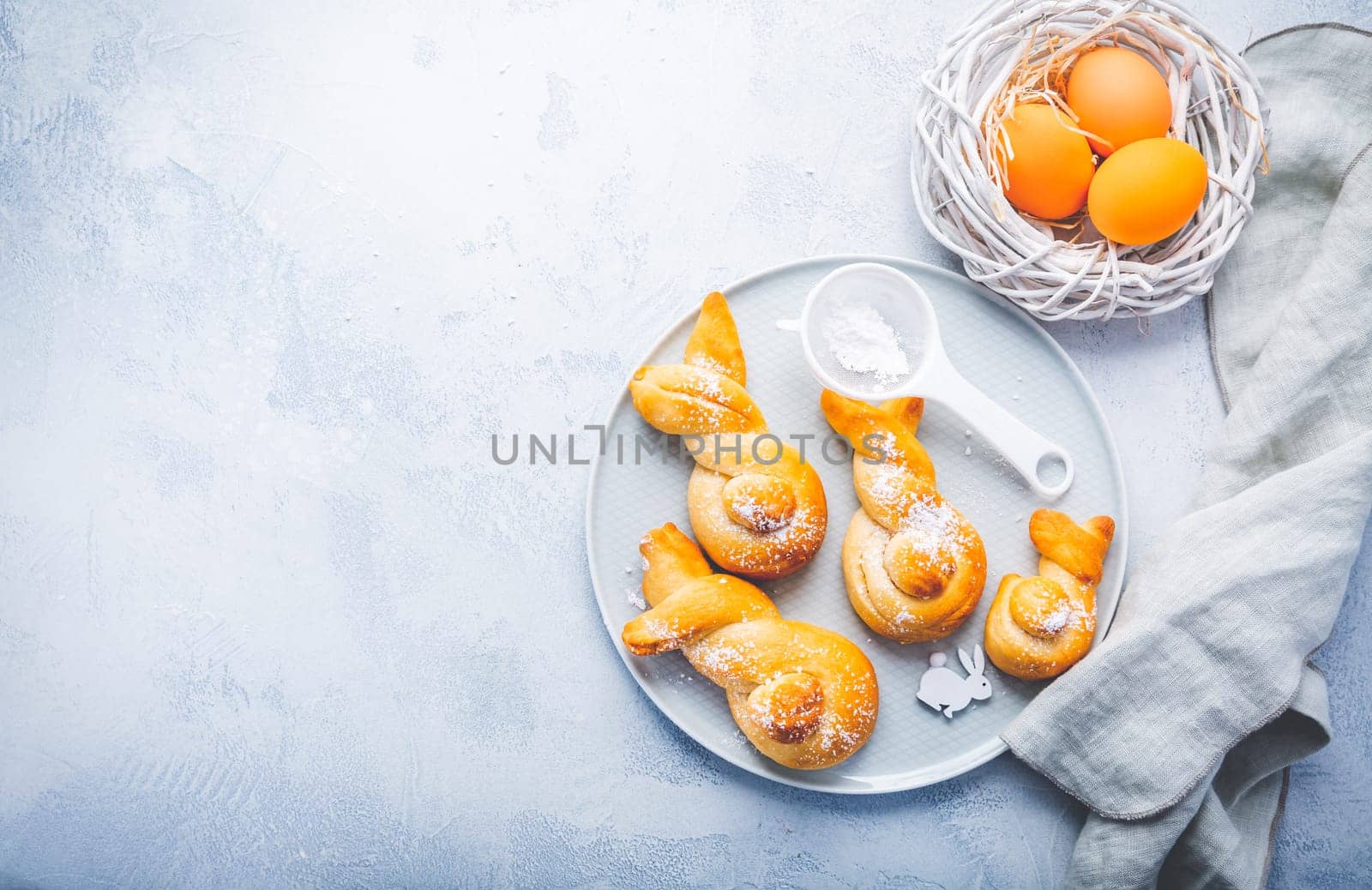 Buns made from yeast dough in a shape of Easter bunny and colored eggs