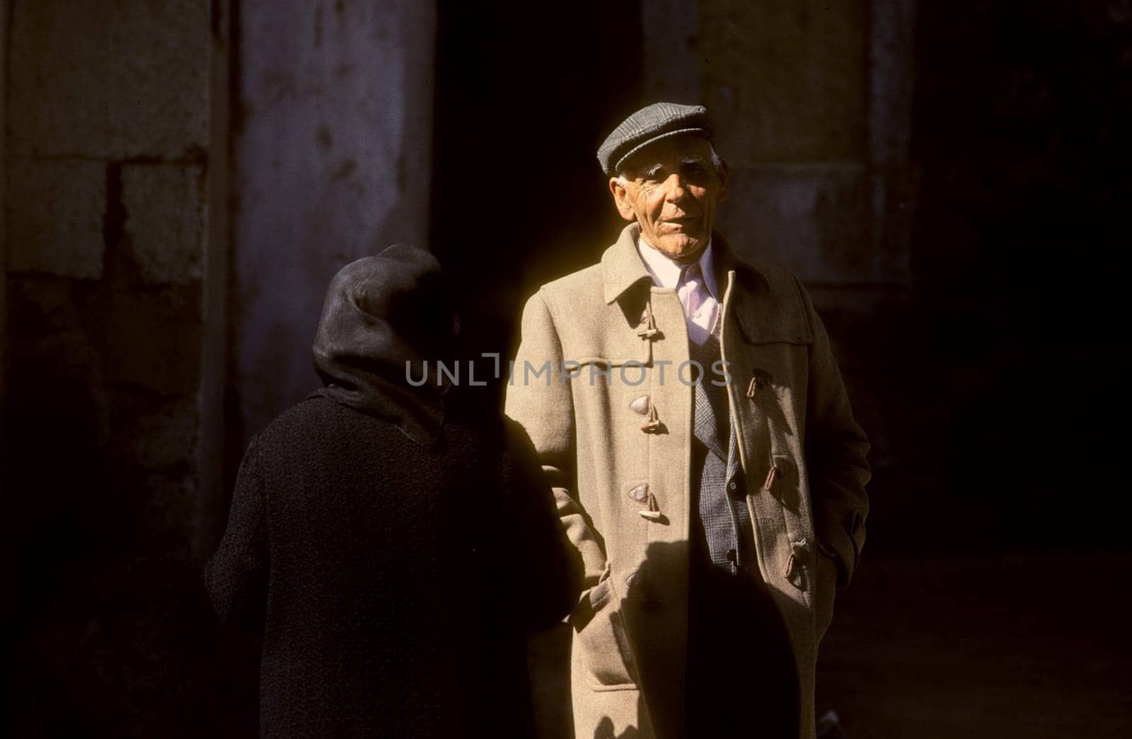Lisbon, Portugal - July 4, 1992: portrait of old man in camelhair suit and backside of old lady in shadow.
