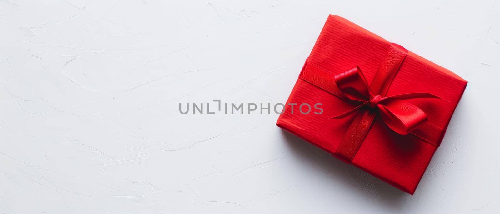 A vibrant red gift box with a satin ribbon lies on a textured white surface, evoking feelings of anticipation and celebration