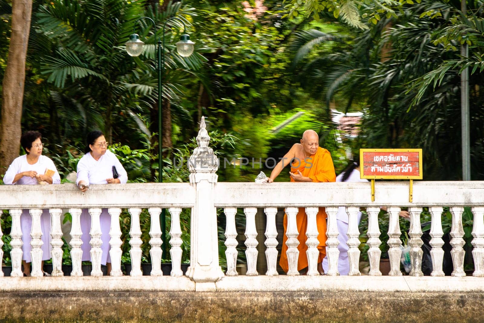 Bangkok, Thailand - December 26, 2007: women in white clothes and orange dressed monk throw blossons into the river to honor the godness
