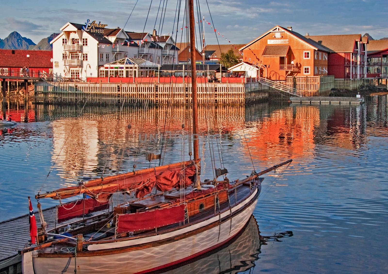Svolvaer, Norway - July 7, 2009: sunset light at harbor and pier of Svolvaer with view to hotels in traditional wooden architecture and historic boat.