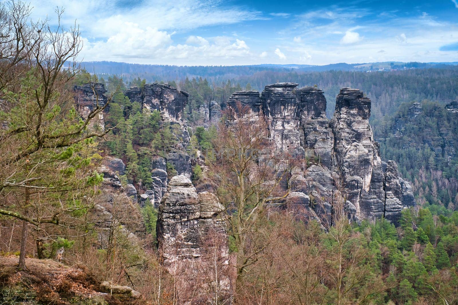 Jagged rocks at the Basteibridge. Wide view over trees and mountains. Dramatic sky. National park in Germany