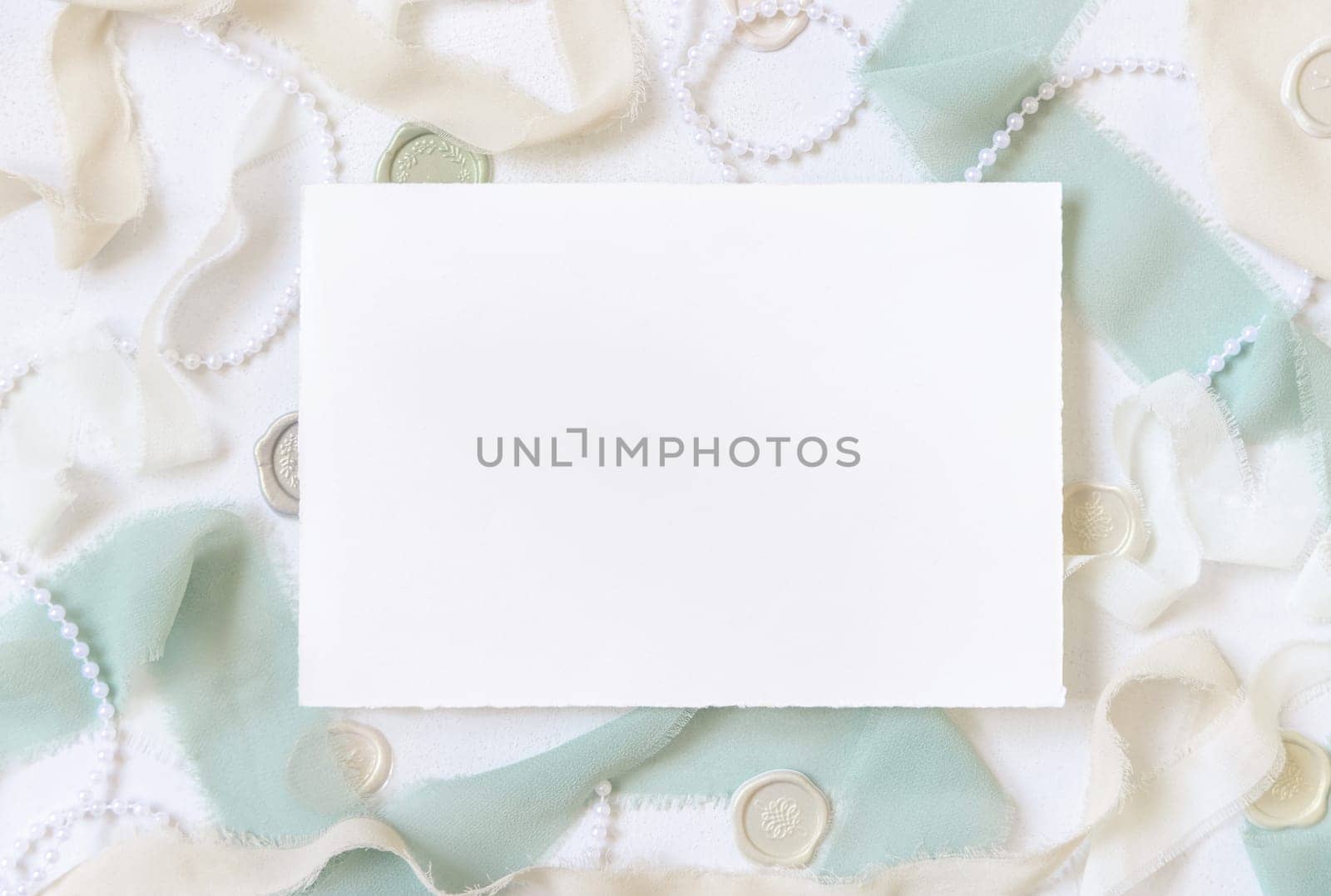 Card near light green and beige silk ribbons and decor on white table top view, Wedding mockup. Romantic scene with horizontal blank card. Valentines, Spring or Mothers day stationery