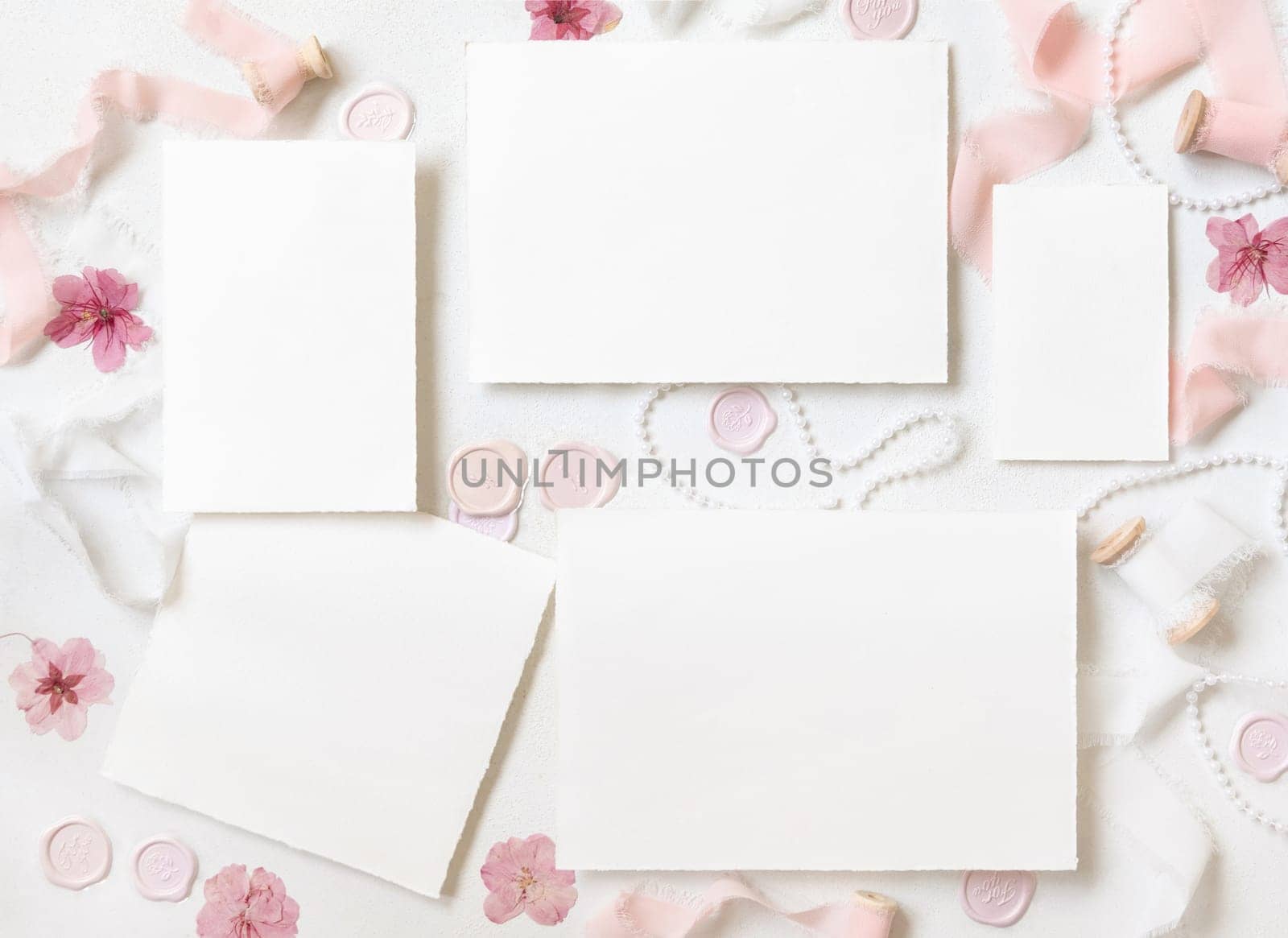 Paper cards near pink decor, flowers, seals and silk ribbons on white table top view, wedding suite mockup. Romantic scene with blank cards flat lay. Valentines, Spring or Mothers day concept