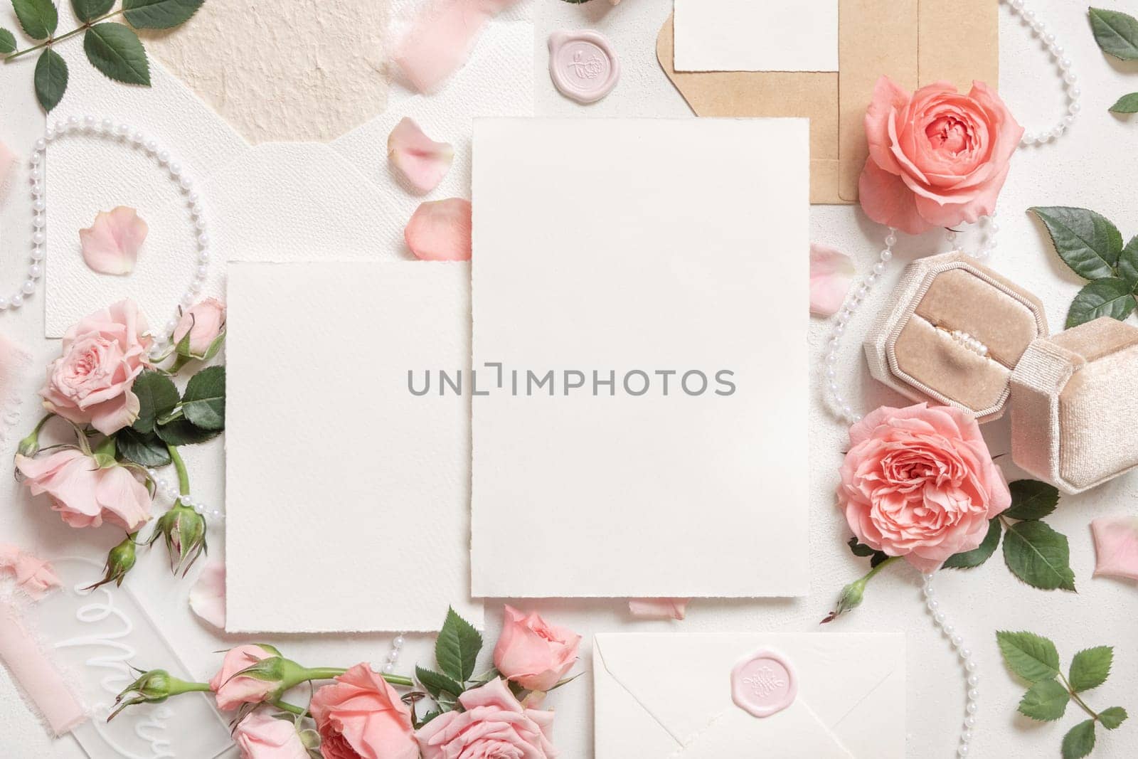 Blank cards near light pink roses, engagement ring in a box and silk ribbons on white table top view, wedding mockup. Romantic flat lay with vertical cards and pastel decor