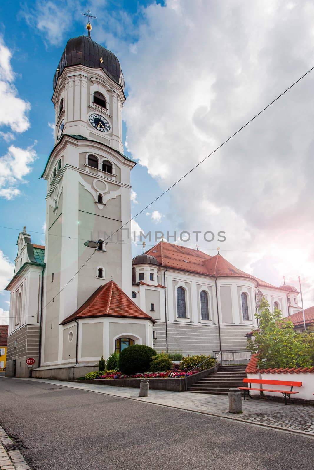 North-side wide angle view of the St. Andreas Church in Nesselwang / Bavaria from in front of a blue sky with large white clouds with lens flares in the summer of 2023.