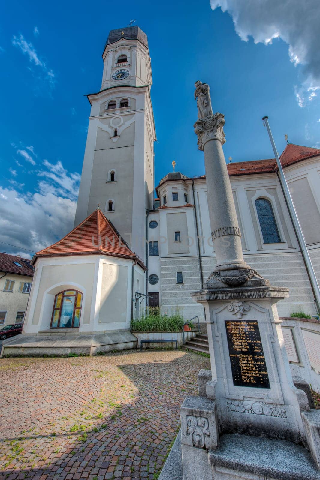 Nesselwang, Germany - July 06, 2023: Wide angle view of the north side of the Saint Andreas Church with the war memorial in the foreground.ummer 2023.