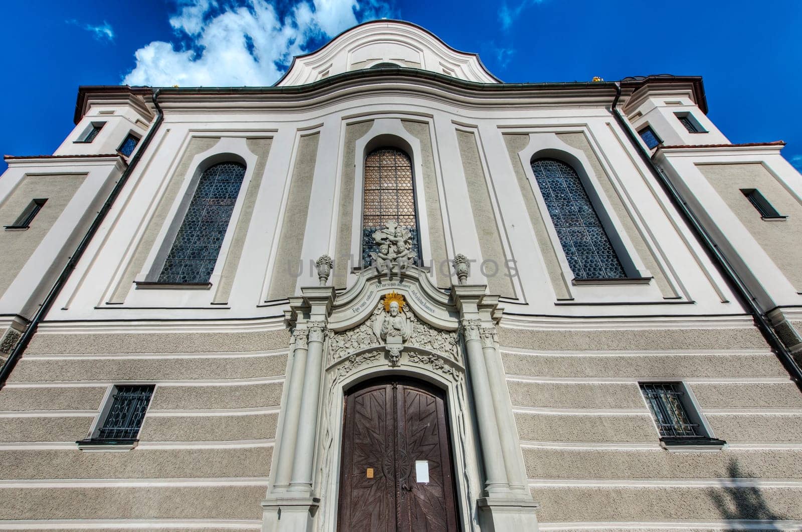 Nesselwang, Germany - July 06, 2023: Steep wide-angle view of the entrance portal of the Saint Andreas Church from the west against a blue sky with individual white clouds.