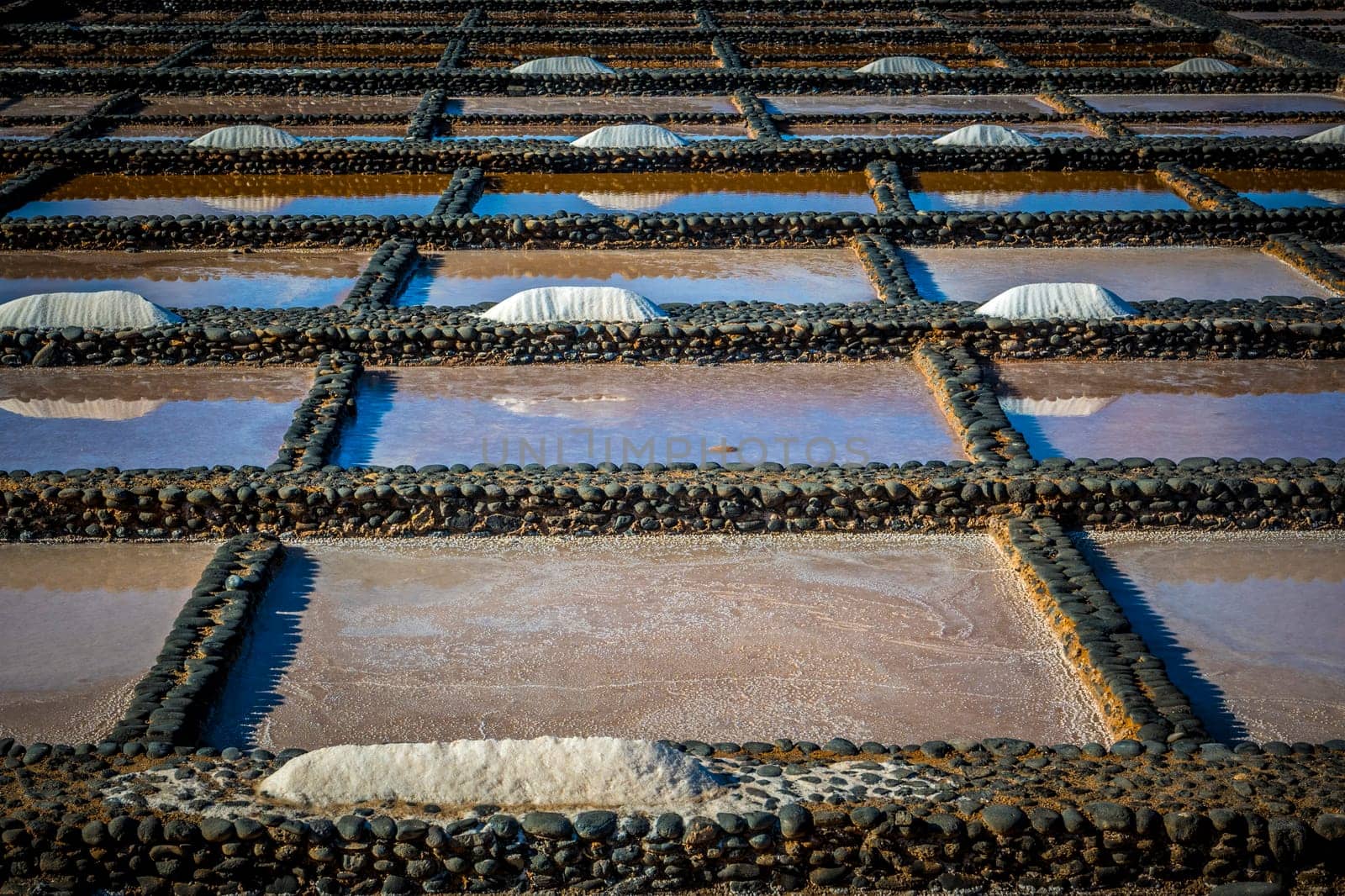 View on traditional rectangular salt evaporation ponds or salt pans creating a grid showing different stages of evaporation and concentration.
