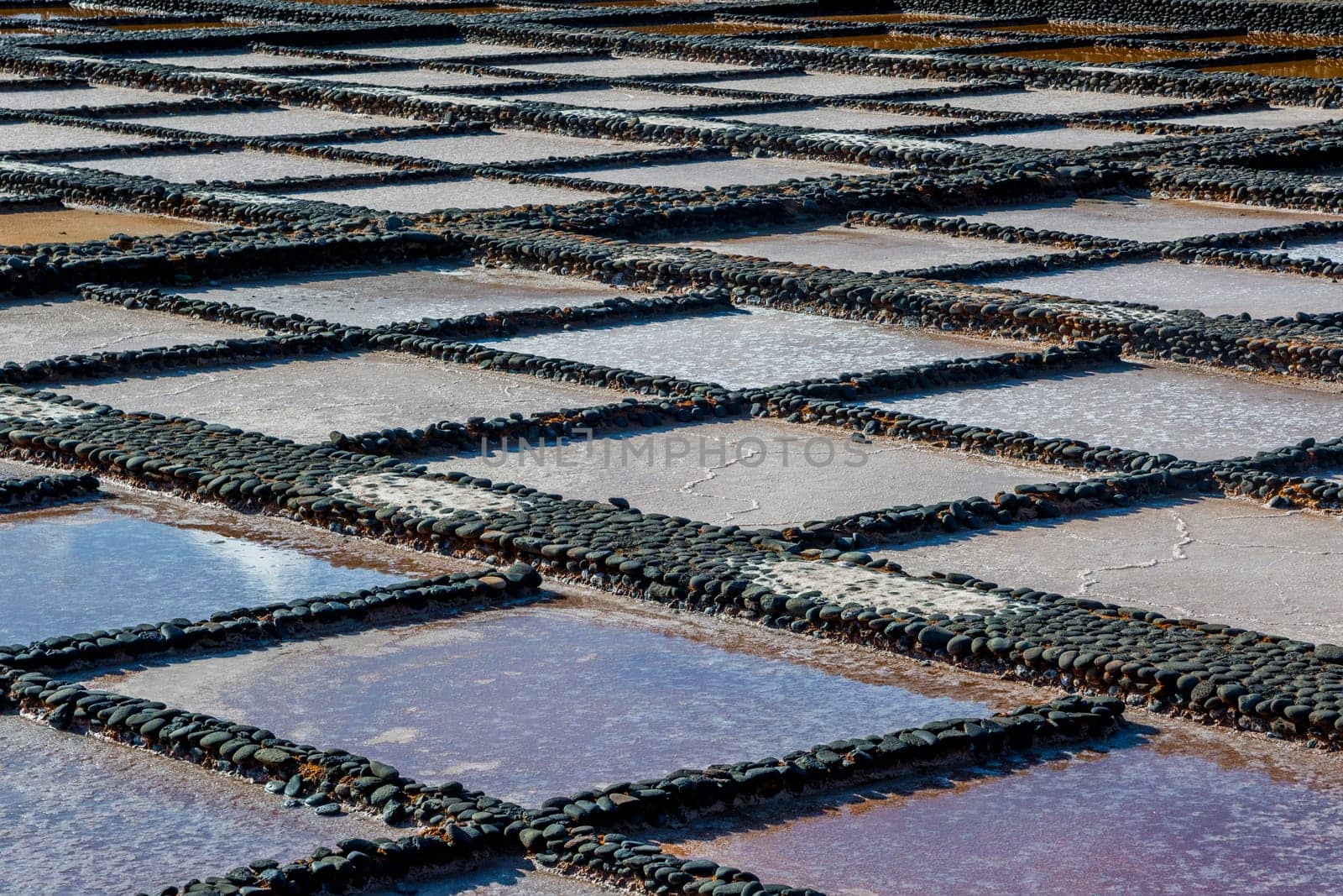 View on traditional rectangular salt evaporation ponds or salt pans creating a grid showing different stages of evaporation and concentration.