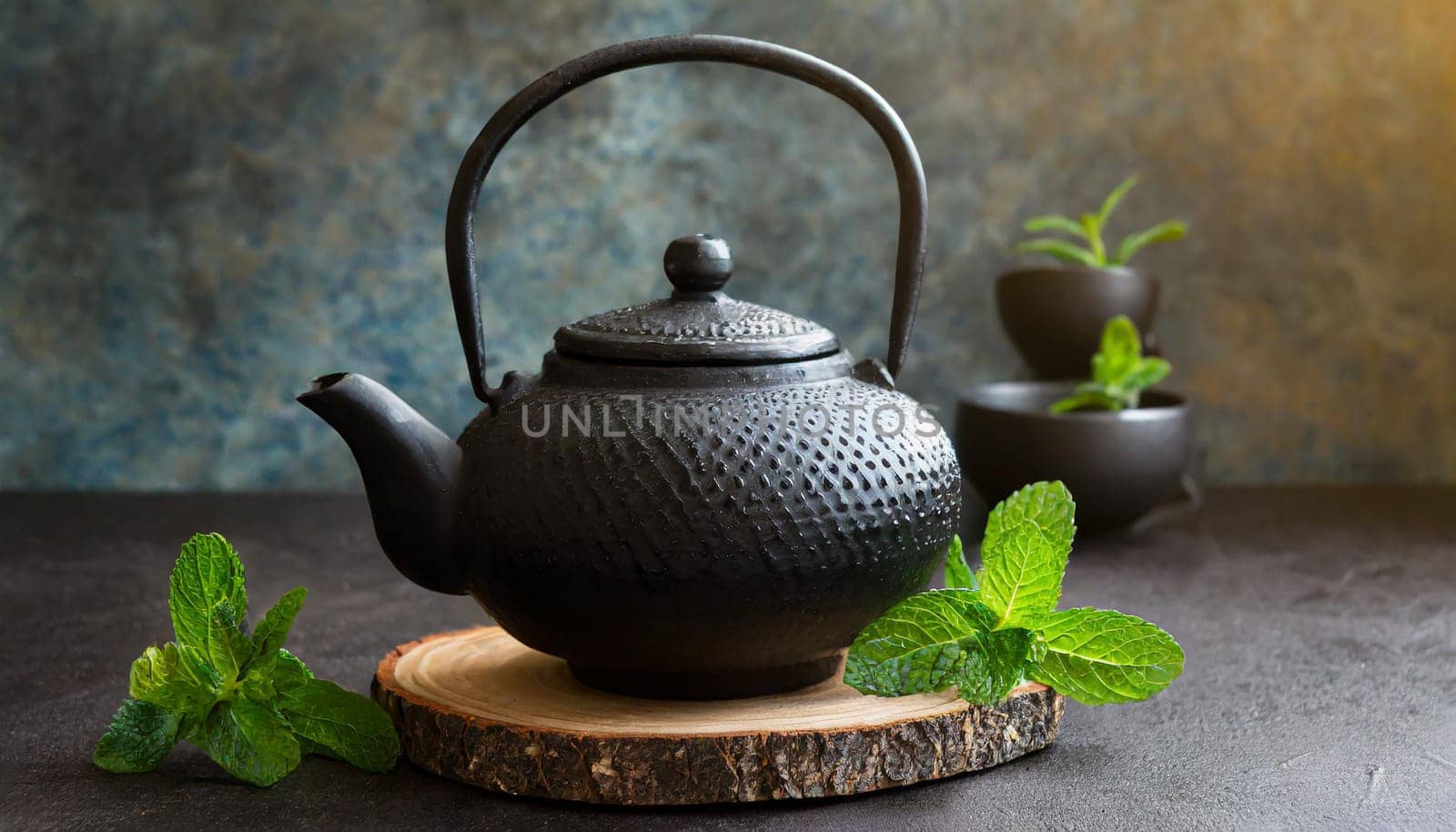 Black iron Asian teapot with sprigs of mint for tea
