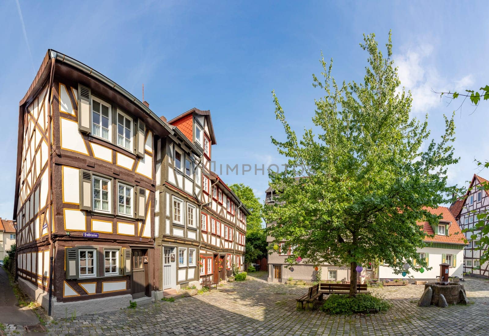 Alsfeld, Germany - June 25, 2021: famous half timbered historic houses at central square with tree and bench in Alsfeld, Germany.